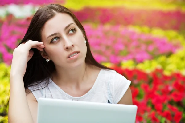 노트북과 꽃 침대에 앉아 웃는 소녀 — 스톡 사진