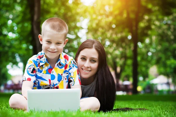 Lächelnd liegen Mutter und Sohn mit Laptop im Gras — Stockfoto