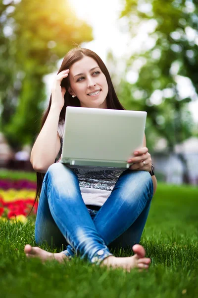 노트북으로 잔디에 앉아 웃는 소녀 — 스톡 사진