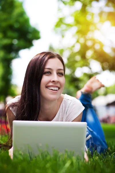 Smiling girl laying on grass with laptop — Stock Photo, Image