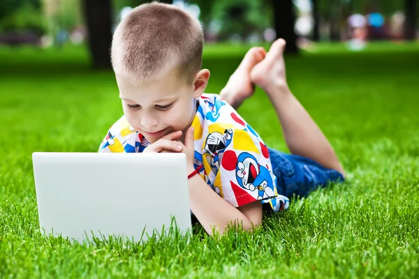 Schattige kleine jongen liggen met een laptop op het gras — Stockfoto