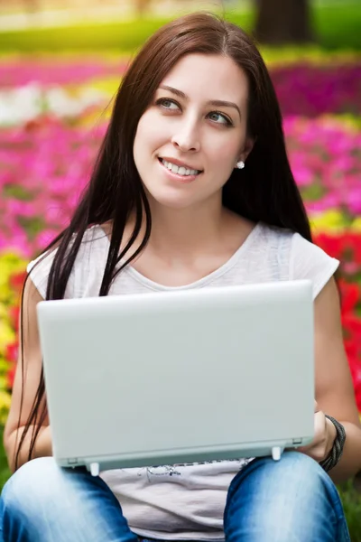 Leende flicka sitter i blomma säng med laptop — Stockfoto