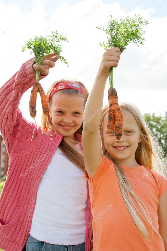 Two young girls holding fresh carrots