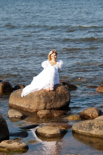 Woman sitting on the stone on the seashore — Stock Photo, Image