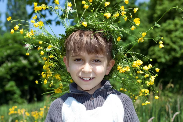 Retrato de un niño joven con una corona de flores amarillas en la cabeza — Foto de Stock