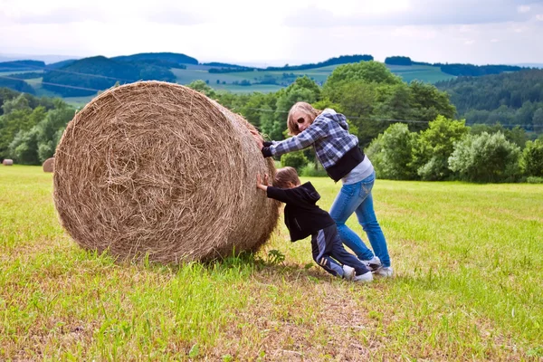 A girl and a boy pushing a round bundle of straw. — Stock Photo, Image