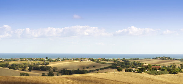 Panorama view of italian countryside with the sea, blue sky and puffy clouds in the background