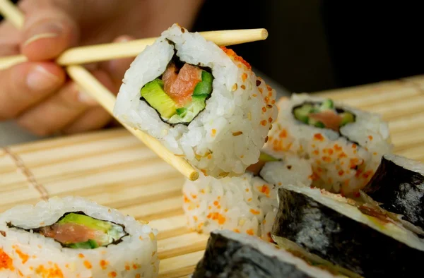 Mão segurando sushi japonês. Guardanapo de bambu no fundo — Fotografia de Stock
