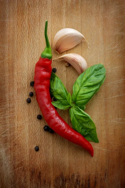 Red chili peppers, garlic and basil over a wooden background — Stock Photo, Image