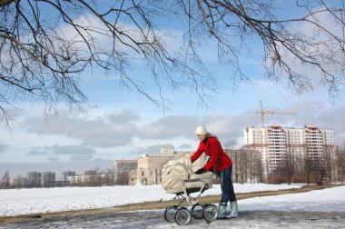 Wide shot of happy young mother in red coat with baby in buggy clipart