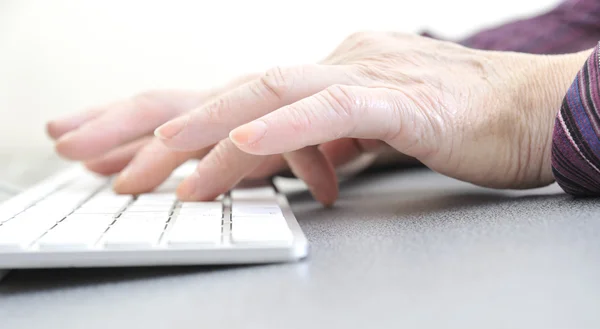 Handen van een oude vrouw te typen op het toetsenbord, geïsoleerde op wit, close-up. — Stockfoto