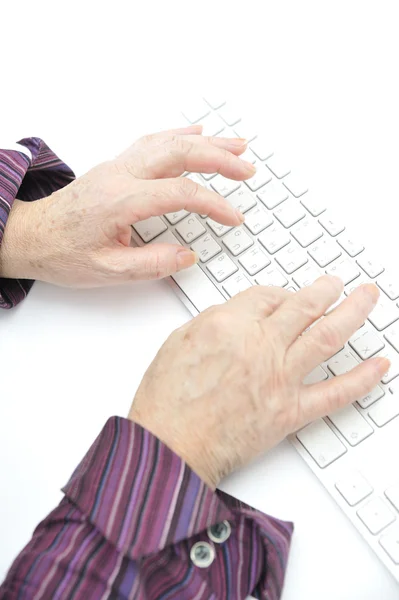 Ręce starej kobiety, wpisując klawiatury, biały na białym tle na zbliżenie. — Zdjęcie stockowe