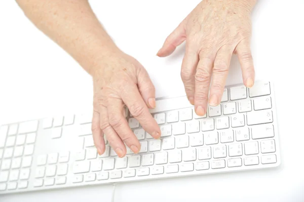 Ręce starej kobiety, wpisując klawiatury, biały na białym tle na zbliżenie. — Zdjęcie stockowe