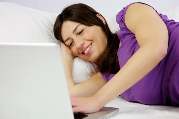 Mulher atraente lê seu laptop deitado na cama — Fotografia de Stock