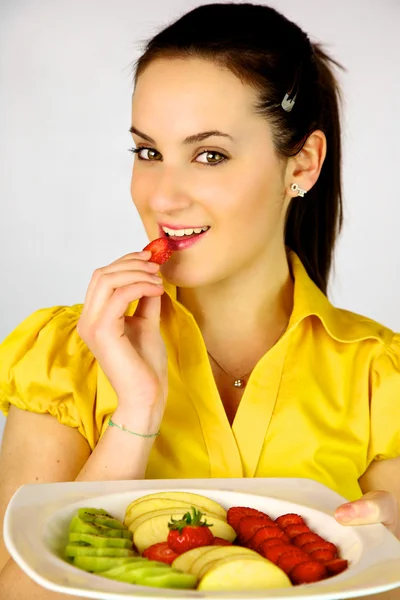 Modelo femenino con plato con fruta comiendo fresa —  Fotos de Stock
