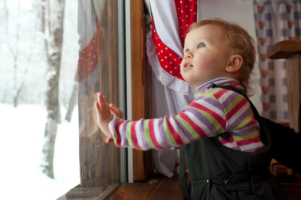 Het kleine meisje is kijkt uit het raam — Stockfoto
