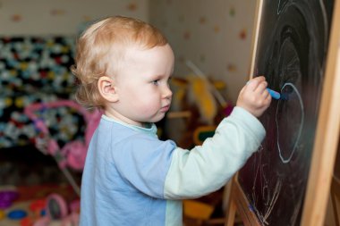 küçük kız, bir tahtaya tebeşir ile çizer.