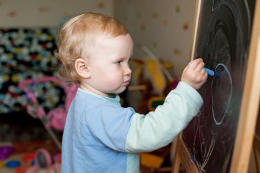 Little girl draws with chalk on a blackboard clipart