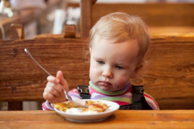 Blond babe eats pancakes at a wooden table clipart