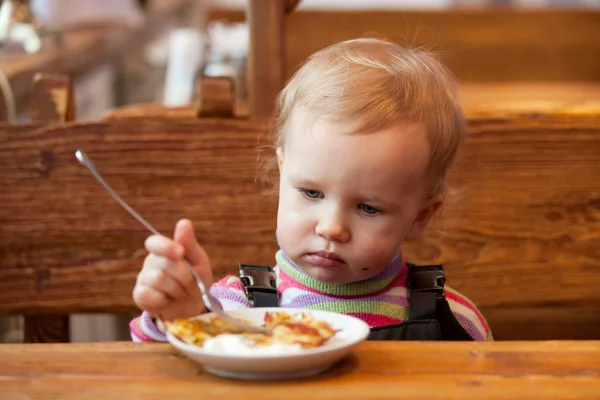 金髪の赤ん坊は木製のテーブルでパンケーキを食べる — ストック写真