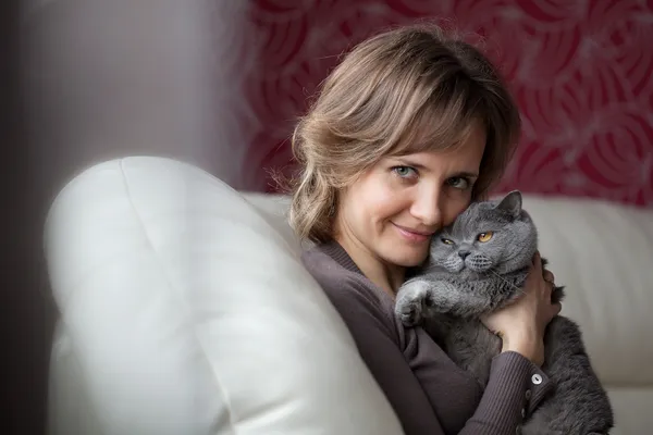 Kobieta siedzi na kanapie i pieści szary kot — Zdjęcie stockowe