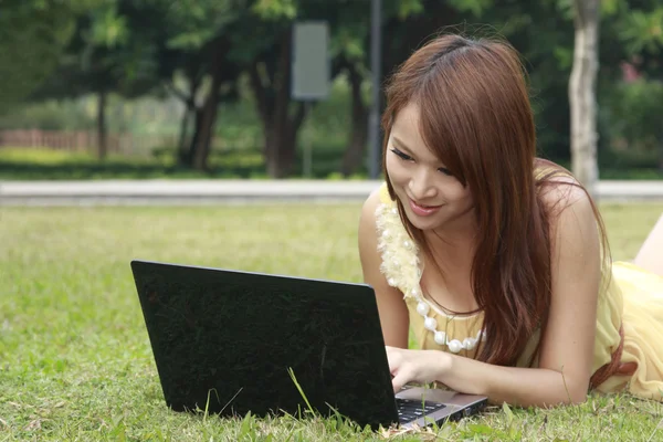 Menina asiática feliz usando laptop na grama — Fotografia de Stock