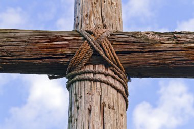 Closeup of a rugged wooden Cross and blue, cloudy sky clipart
