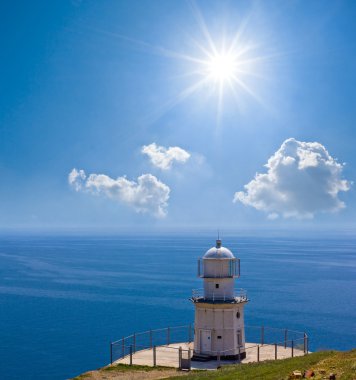 Lighthouse on a marine cape by a sunny day clipart