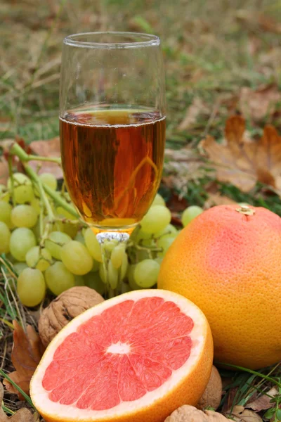 Sklenka bílého vína mezi ovoce v trávě — Stock fotografie