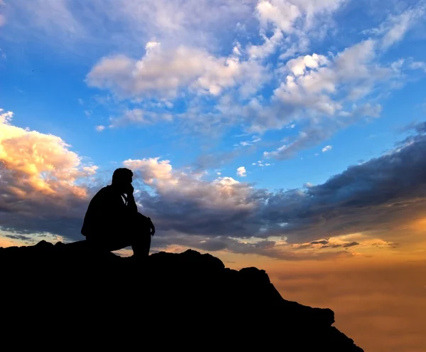 Bir akşam gökyüzü arka plan üzerinde oturan adam siluet — Stok fotoğraf