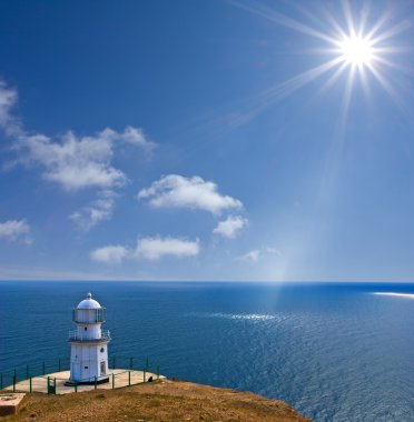 Lighthouse on a sea coast under a sparkle sun clipart