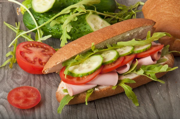 Sandwich mit Schinken, Tomate, Gurke und Rucola auf dem alten Holzschneidebrett — Stockfoto