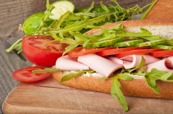 Smörgås med skinka, tomat, gurka, ruccola på gamla trä skärbräda — Stockfoto