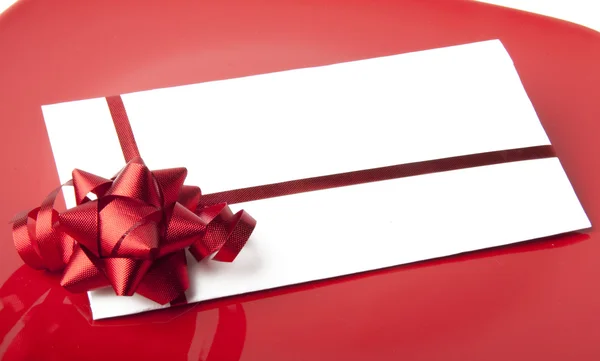 Nahaufnahme eines weißen Umschlags mit roter Schleife auf rotem Hintergrund — Stockfoto