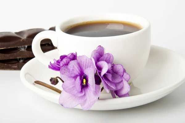 Šálek kávy, čokolády a fialky na stůl bílý — Stock fotografie
