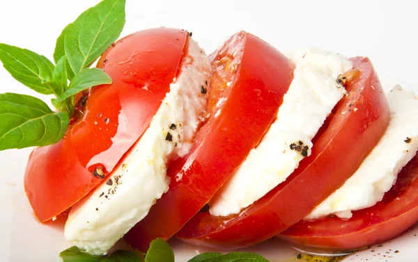 Rodajas de tomate y mozzarella decoradas con hojas de albahaca en un plato y whi — Foto de Stock