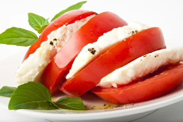 Rodajas de tomate y mozzarella decoradas con hojas de albahaca en un plato y whi —  Fotos de Stock