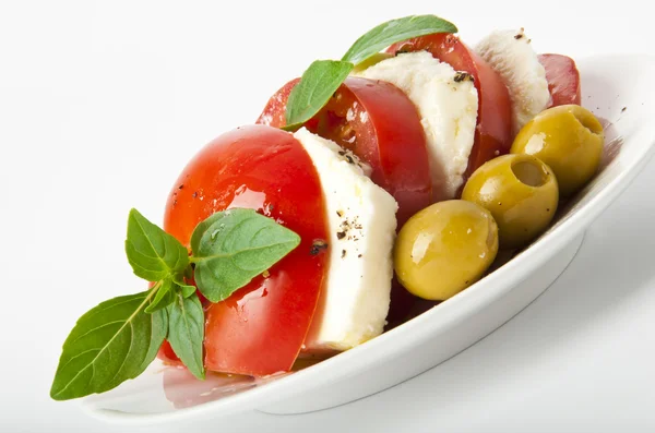 Plastry pomidorów i mozzarelli, urządzone z liści bazylii na płytkę i whi — Zdjęcie stockowe