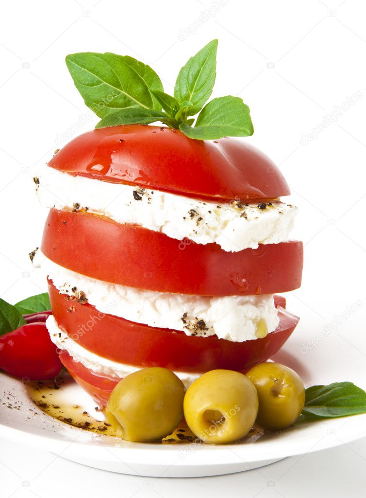 Tomato and mozzarella slices decorated with basil leaves on a plate and whi