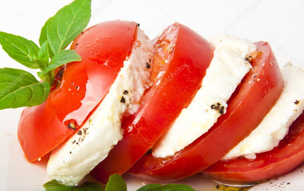 Tomato and mozzarella slices decorated with basil leaves on a plate and whi
