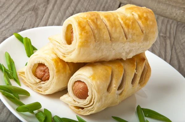 Sausage in the dough on a plate with greens — Stock Photo, Image