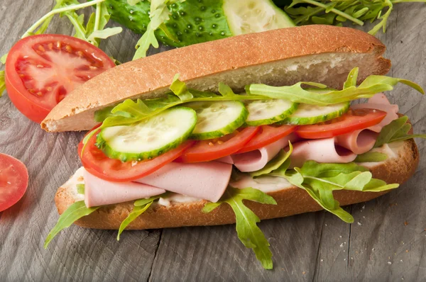 Sandwich mit Schinken, Tomate, Gurke und Rucola auf dem alten Holzschneidebrett — Stockfoto