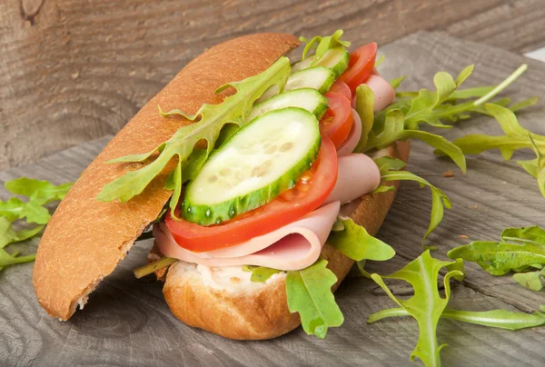 Jambon, domates, salatalık, roka eski ahşap kesme tahtası üzerinde sandviç — Stok fotoğraf
