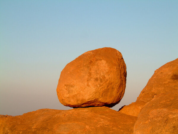 Huge granite boulder perched on rocks against blue sky
