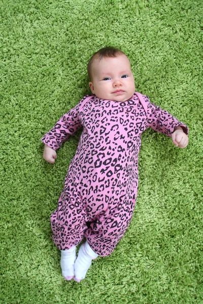 Ребенок лежит на спине на зеленом ковре в розовом леопардовом костюме — стоковое фото
