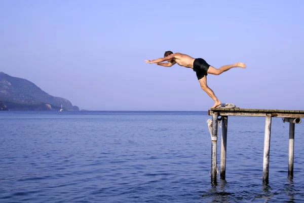 Muž skok, potápění do moře z mola — Stock fotografie