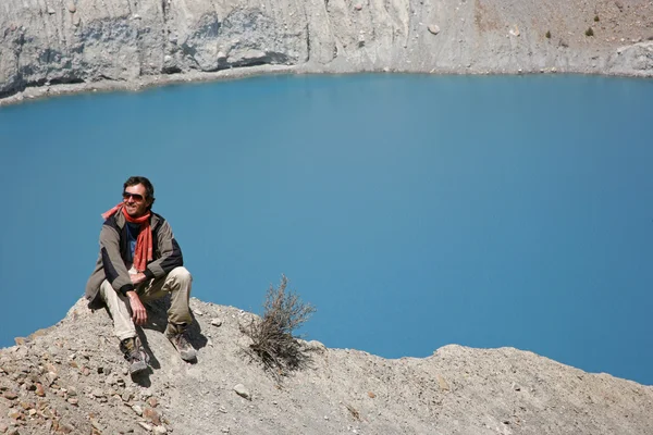 Trekker siedzi na szczycie góry z Błękitne jezioro w tle — Zdjęcie stockowe