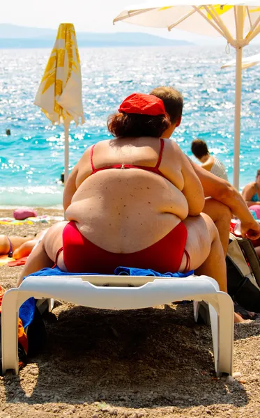 Obézní žena sedí na lehátku na pláži v Chorvatsku — Stock fotografie