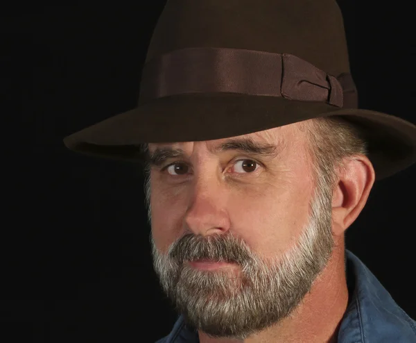 Un hombre barbudo en un sombrero sonríe ligeramente — Foto de Stock