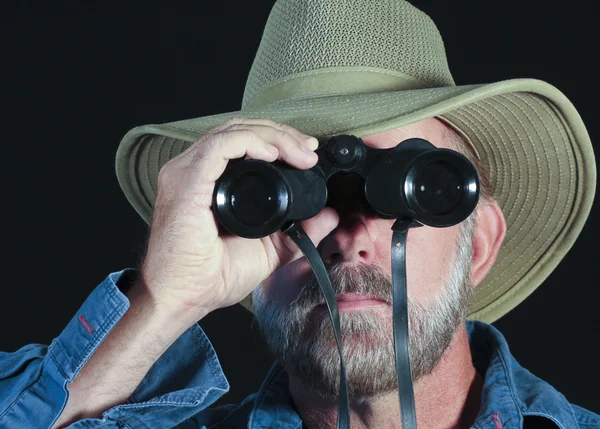 Een man in een safari hoed ziet er door middel van verrekijkers — Stockfoto